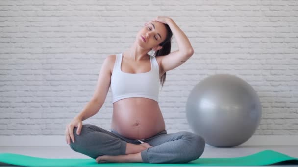 Hübsche junge schwangere Frau dehnt sich nach Pilates-Übungen im Klassenzimmer vor der Geburt. — Stockvideo