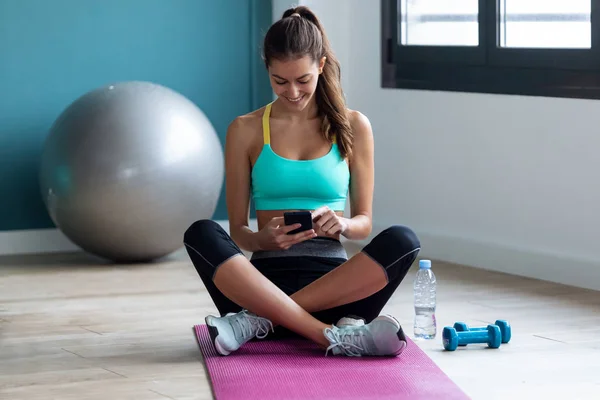Mujer joven deportiva usando su teléfono móvil mientras está sentada después de una clase de pilates en el gimnasio . —  Fotos de Stock