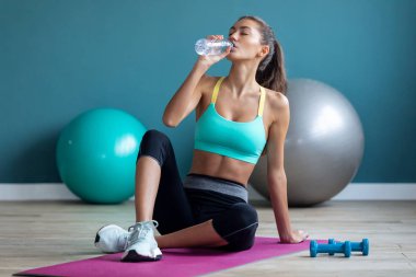 Spor salonunda pilates yaparken su içen genç bir kadın..