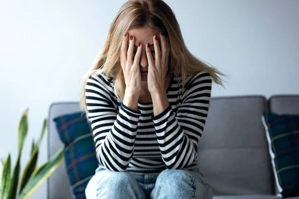 Wanita muda yang tertekan memikirkan masalah-masalahnya sambil duduk di sofa di rumah . — Stok Foto