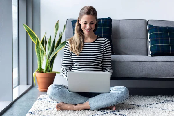 Mujer bastante joven usando su computadora portátil mientras está sentada en el suelo en casa . —  Fotos de Stock