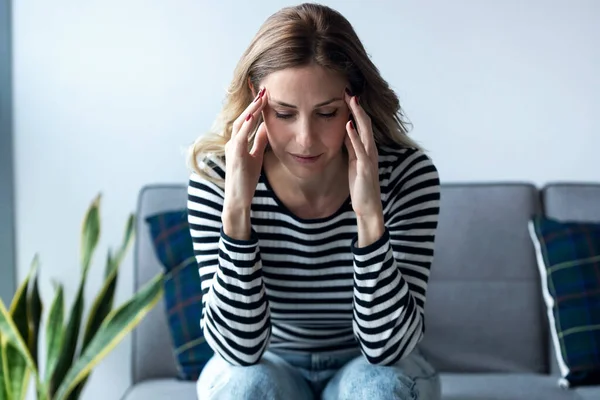 Ung kvinna med huvudvärk sitter på soffan i vardagsrummet hemma. — Stockfoto