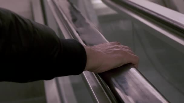 Gros plan d'une main masculine sur la main courante en caoutchouc noir d'un escalator en descendant . — Video