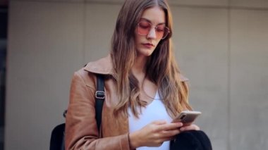 Video of pretty young woman using her mobile phone while standing in the street.