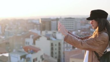 Video of pretty young woman taking photographs of city on the rooftop.