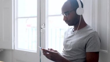 Video of black young man listening to music with headphones and using the smartphone at home.