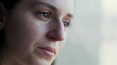 Video of sad young woman crying while looking through the window at home.