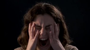 Video of a young woman close-up screaming on black background. Mental illness concept.