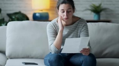Video of worried young woman thinking about her problems while holding bills of home.