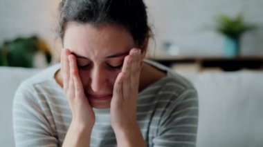 Video of depressed young woman thinking about her problems while sitting on the sofa at home.