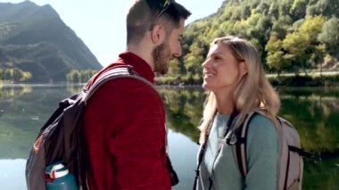 Video of two travel hikers in love kissing in front of the lake in mountain.