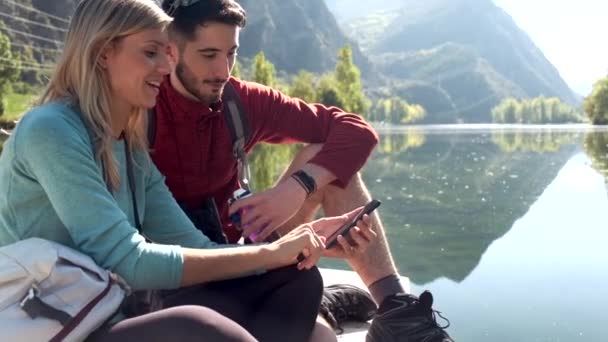 Video Due Escursionisti Che Utilizzano Cellulare Seduti Fronte Lago Montagna — Video Stock