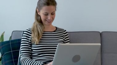 Video of pretty young woman using her laptop while sitting on sofa at home.