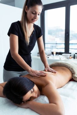 Genç bir kadının güzellik merkezindeki güzel bir kadına vücut tedavisi için doğal malzemelerle çikolata kremi sürmesi..