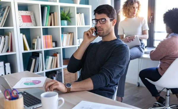 사업가가 노트북을 쓰면서 휴대폰으로 얘기하는 장면입니다 사무실에서 동료들 일하는 모습입니다 — 스톡 사진