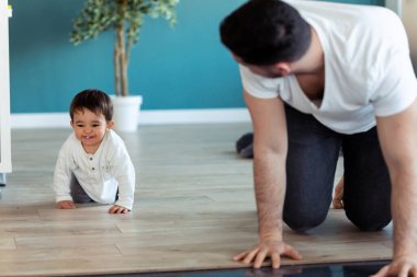 Gülümseyen genç baba, evde yerde sürünürken küçük bebekle eğleniyor..