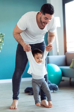 Yakışıklı, genç bir babanın bebeğiyle birlikte oynayıp evde eğlendiği bir fotoğraf..