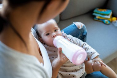 Evdeki kanepede otururken annesinin bebeğini biberonla beslediği yakın plan..