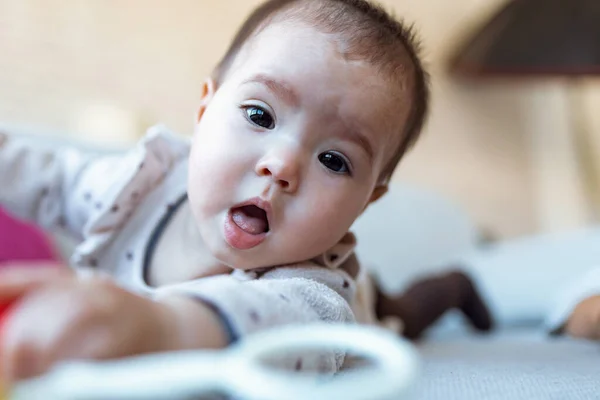 Strzał Cute Baby Girl Patrząc Kamerę Bawiąc Się Grzechotką Leżąc — Zdjęcie stockowe