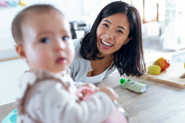 幸せな若いです母のショットとともに彼女の赤ん坊娘見ますカメラでザ台所にホーム — ストック写真