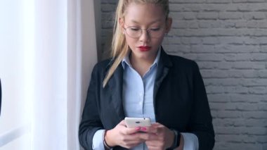 Ofisteki pencerenin yanında dururken cep telefonunu kullanan zarif genç bir iş kadını..