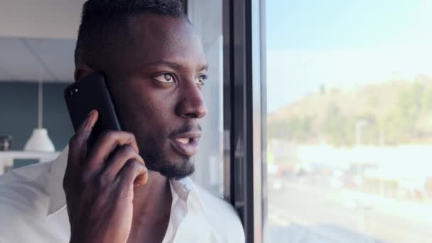 Jovem de negócios falando no celular enquanto olha através de uma janela no escritório . — Vídeo de Stock