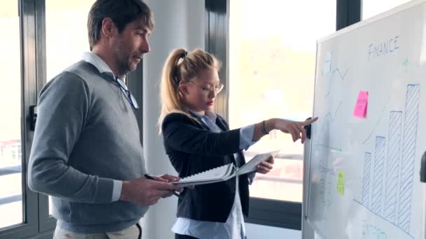 Hombre de negocios guapo explicando el proyecto con pizarra blanca a su colega en el lugar de coworking . — Vídeo de stock