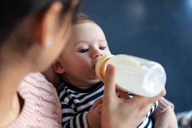 Anne, evdeki kanepede otururken bebeğini biberonla besliyor..