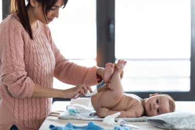 Konsantre olmuş genç bir annenin evdeki küçük oğluna bezini değiştirmesi..