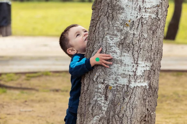 Tiro Menino Engraçado Jogando Enquanto Ele Está Abraçando Uma Árvore — Fotografia de Stock