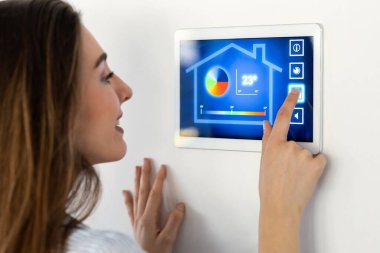 Güzel bir genç kadının dijital tablet üzerindeki ev otomasyon sistemini kullanarak ısıyı düzenlerken görüntüsü..