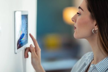 Güzel bir genç kadının dijital tablet üzerindeki ev otomasyon sistemini kullanarak ısıyı düzenlerken görüntüsü..