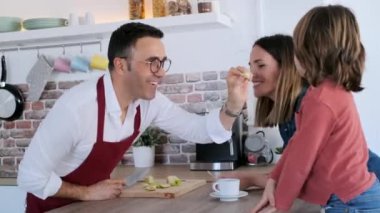 Yakışıklı bir babanın mutfakta elma keserken karısıyla ve oğluyla eğlendiği bir video..