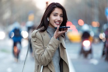 Güzel bir genç kadının sokakta dikilirken akıllı telefonunda ses tanıma sistemi kullanması..
