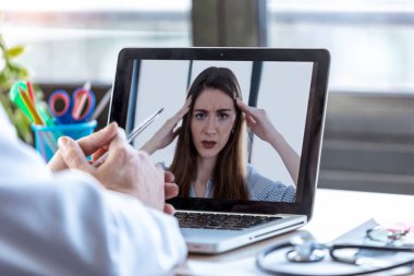 Evdeki bilgisayarla bir kadın hastayla ilgilenen bir doktorun görüntüsü..