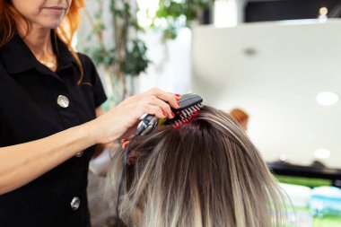Kuaförünün, kuafördeki kadın müşterisinin saçlarının uzaması için ultrasonik ve kızılötesi lazer tarağıyla tedavi uyguladığı yakın plan..