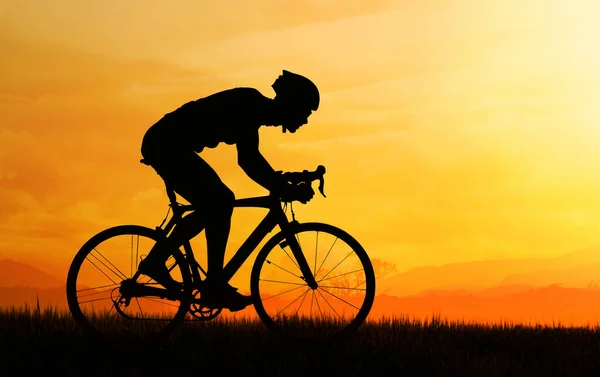 Double exposure of silhouette of cyclist riding in the field and orange sunset sky.