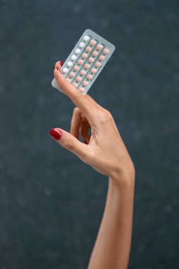 Kadın elinin karanlık bir arka plana karşı doğum kontrol haplarını tutarken yakın plan..