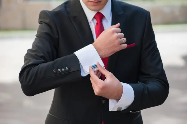 siyah elbiseli bir adam onun kol düğmeleri düzeltiyor.