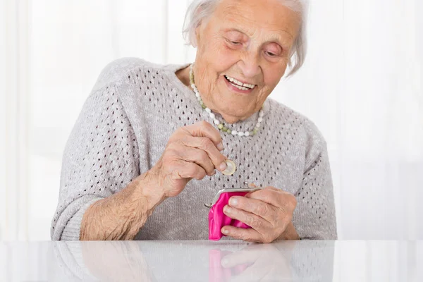 Старшая женщина вставляет монету в кошелек — стоковое фото