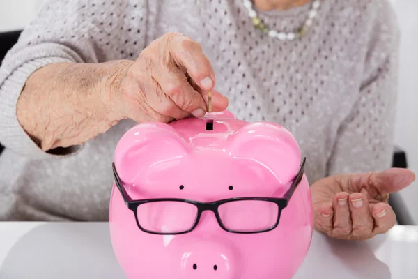 Mujer mayor mano insertando monedas en Piggybank — Foto de Stock