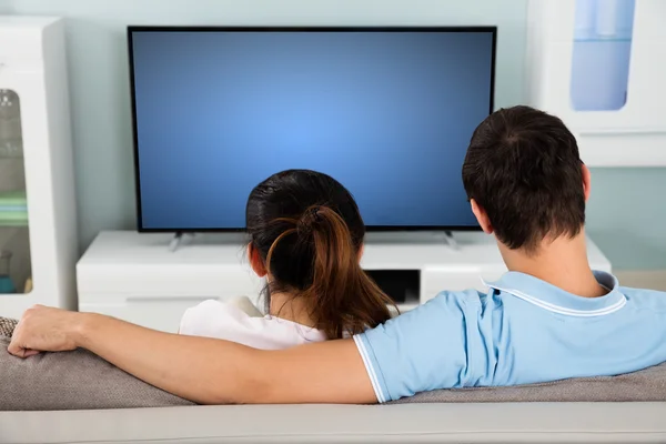 Ζευγάρι που κάθεται στον καναπέ μπροστά από την τηλεόραση — Φωτογραφία Αρχείου