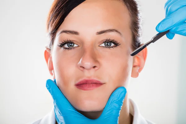 Рука хирурга со скальпелем рядом с лицом женщины — стоковое фото