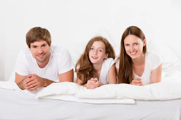 Sonriente familia acostada en la cama — Foto de Stock