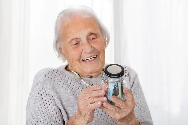 Старшая женщина смотрит на банку денег — стоковое фото