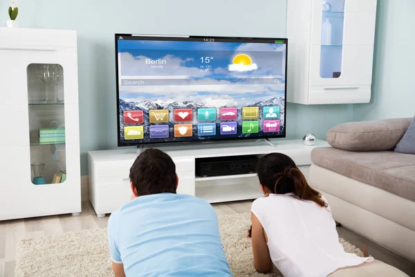 Pareja acostada en la alfombra viendo la televisión —  Fotos de Stock