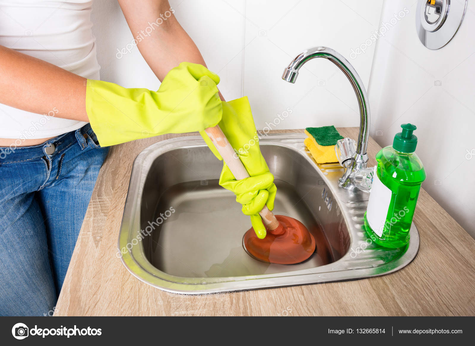 Woman Using Plunger In Kitchen Sink Stock Photo