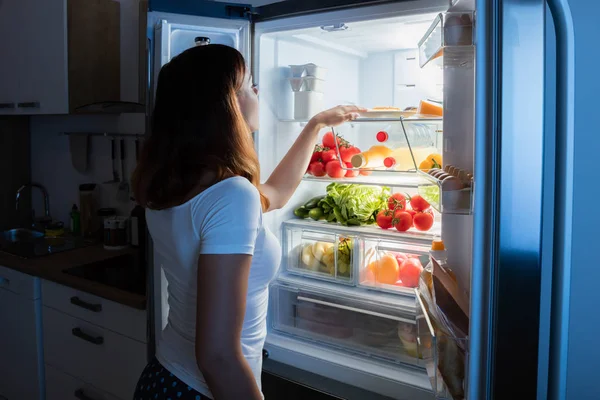 Жінка дивиться на їжу в холодильнику — стокове фото