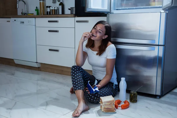 Woman eats in front of refrigerator — Stock Photo, Image