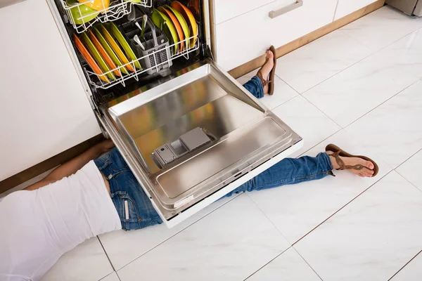 Woman  lying under dishwasher — Stock Photo, Image